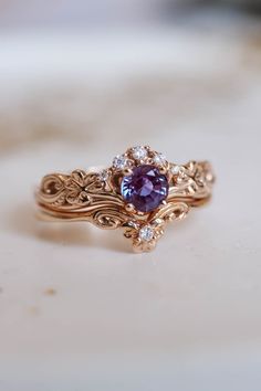 a close up of a ring with a purple stone in the center and diamond accents