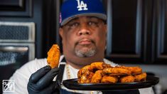 a man holding a black plate with fried food on it and wearing a baseball cap