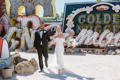 This vibrant couple is all smiles at the iconic Neon Museum! 🌟 The bride, in her elegant, simple wedding dress flowing into a gentle train, looks stunning with her loose waves and bouquet of white flowers. The groom's classic black tux completes their timeless look. Mid-stride and holding hands, they're perfectly framed by colorful vintage Vegas signs, adding a playful and nostalgic touch. 💖✨ #weddingideas #timelessweddingdress #lasvegaswedding #neonmuseum #vintagewedding Las Vegas Engagement Photos, Las Vegas Wedding Photos, Vegas Wedding Photos, Married In Vegas, Vegas Weddings