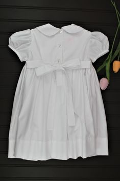 This classic dress is perfect for weddings, christenings, or blessings. The smocking on the bodice is accented with white pearls. 65% Polyester - 35% Cotton Machine wash 3 Button back closure Elegant Smocked Dress With Smocked Cuffs For Baptism, Classic Daywear Dress With Smocked Bodice, Elegant Smocked Ruffle Dress For Baptism, Classic White Smocked Dress For Spring, Classic Fitted Dress For Baptism, Classic Dresses With Smocked Back For Daywear, Fitted Classic Smocked Dress, Elegant Fitted Smocked Dress, Classic Daywear Dresses With Smocked Back