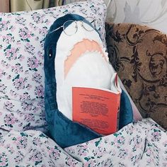 an open book in the pocket of a shark pillow on a bed with floral sheets