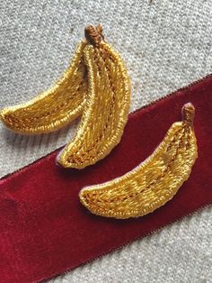 two golden bananas are sitting on a red velvet ribbon with gold sequins attached to them