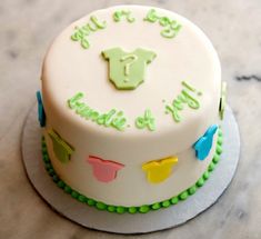 a white cake with green frosting and baby clothes on it's top, sitting on a marble surface