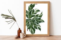 a green leafy plant in a wooden frame next to a brown vase and white wall