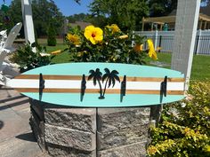 a surfboard with three palm trees on it sitting in front of a flower pot