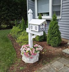 a white mailbox sitting in the middle of a flower bed next to a house