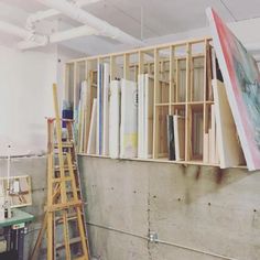 an art studio with various pieces of artwork on the wall and ladders in front of it