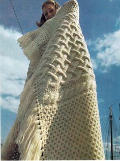 a woman wrapped up in a blanket on top of a sailboat under a cloudy blue sky