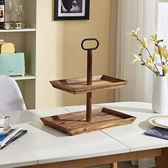 three tiered wooden tray on top of a white table next to a vase with flowers