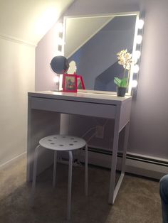 a vanity table with a stool underneath it and a large mirror on the wall behind it