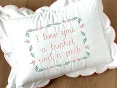 two white pillows with embroidered words on them sitting on a wooden floor next to each other