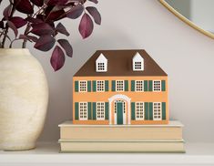 a house sitting on top of a stack of books next to a vase and mirror