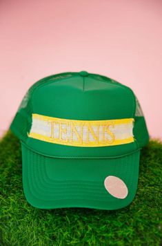 Serve up some style with our Tennis Ribbon Green Trucker Hat! This playful hat features a vibrant green trucker style with an adjustable back for the perfect fit. The yellow and white striped ribbon adds a touch of fun, while the striking Tennis and tennis ball patches add sporty charm. (Game, set, match!) Green Trucker Hat, Game Set Match, Striped Ribbon, Tennis Ball, Vibrant Green, Trucker Hat, Tennis, Perfect Fit, Ribbon