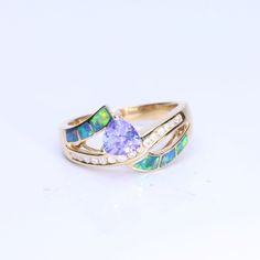 Wear the CIRARI 14K Yellow Gold Inlay Opal Trillion Tanzanite Ring to exude elegance. This ring is incredibly well-made and has a striking trillion-cut tanzanite set in a gorgeous inlay of opals. The design, set in dazzling 14K yellow gold, skillfully combines classic charm with contemporary refinement. This CIRARI masterpiece, a monument to timeless beauty and tasteful design, will elevate your look. Give yourself over to the allure of this magnificent ring. Dazzling Trillion Cut Wedding Rings, Formal Rings With Accent Stones In Trillion Cut, Luxury Trillion Cut Ring With Accent Stones, Formal Ring With Trillion Cut And Accent Stones, Formal Trillion Cut Ring With Accent Stones, Gold Opal Ring With Brilliant Cut As Gift, Gold Opal Ring With Brilliant Cut For Gift, Yellow Gold Opal Ring With Brilliant Cut For Gift, Yellow Gold Opal Ring With Brilliant Cut As Gift