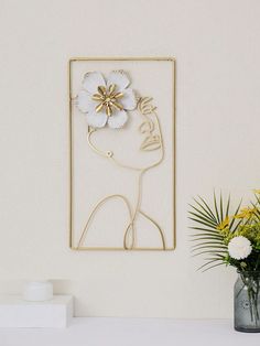 a vase filled with flowers sitting next to a wall mounted art piece on top of a white table