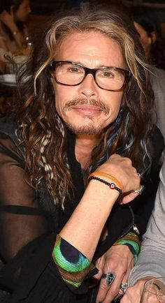 a man with long hair and glasses sitting next to another person at a table in a restaurant