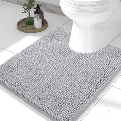 a white toilet sitting next to a gray rug on top of a bathroom floor in front of a sink