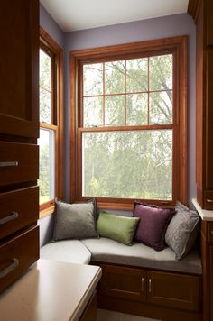 a corner couch in front of a window with wooden trim and pillows on the seat