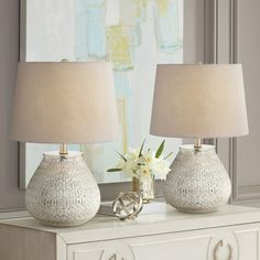 two lamps are sitting on top of a white dresser next to a vase with flowers