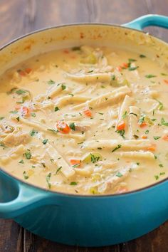 a blue pot filled with chicken noodle soup on top of a wooden table