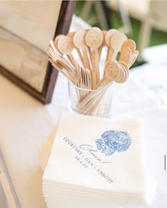 wooden utensils are in a glass vase on a white tablecloth with a blue and white napkin