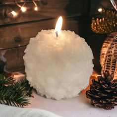 a candle that is sitting on top of a table next to pine cones and christmas lights