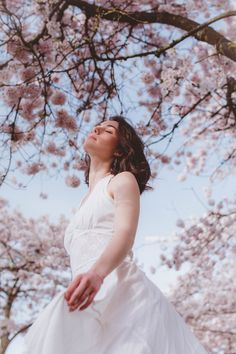 a woman in a white dress standing under a tree with pink flowers