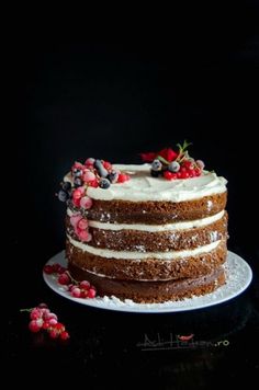 a cake with white frosting and berries on top sitting on a black tablecloth