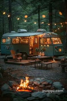 a camper parked in the woods next to a fire pit with lights strung from it