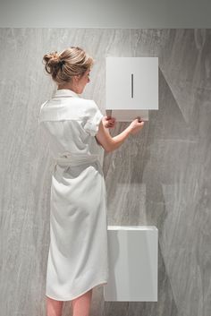 a woman in a white bathrobe holding onto a wall mounted object with the letter i on it