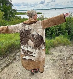 a woman standing on top of a dirt road next to a body of water with her arms outstretched