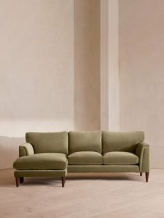 a green couch sitting on top of a hard wood floor next to a white wall