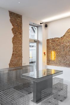 a glass table surrounded by metal cages in a room with exposed brick walls and windows