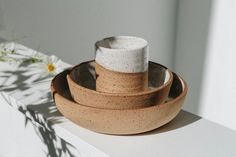 three bowls and one cup sitting on top of a shelf with flowers in the background