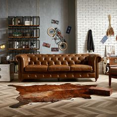 a brown leather couch sitting in a living room next to a white brick wall and wooden floor