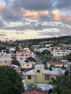 a city with lots of houses and trees in the foreground, under a cloudy sky