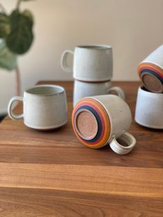 five cups and two mugs are sitting on a wooden table next to a potted plant