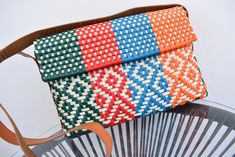 an orange, green, and blue woven purse sitting on top of a metal chair