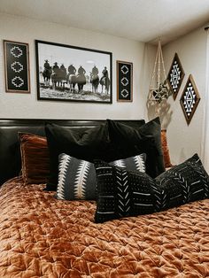 a bed with black and brown pillows in a bedroom next to pictures on the wall