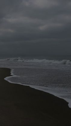 an empty beach with waves coming in to the shore and dark clouds above it on a gloomy day