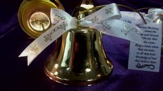 a bell with a white ribbon tied around it and a tag attached to the bell