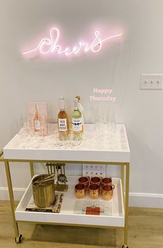 a bar cart with drinks on it in front of a neon sign that says cheers