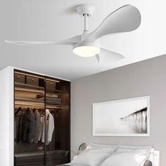 a white bed sitting under a ceiling fan next to a walk in closet with clothes on it