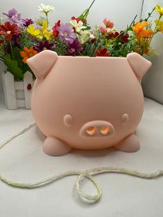 a pink pig shaped planter sitting on top of a table next to some flowers