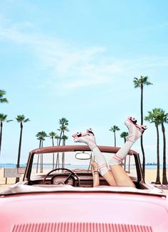 a woman laying on top of a pink car in front of palm trees and the ocean