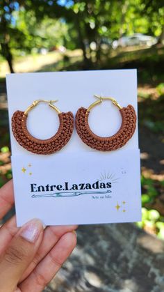 a hand holding up a pair of brown crocheted hoop earrings on top of a card