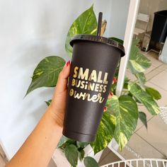 a person holding a coffee cup with the words small business dinner on it, in front of a potted plant