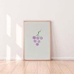 a framed photo with grapes on it in front of a white wall and wooden floor