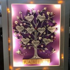 a lighted family tree in a frame with lights on the bottom and hearts hanging from it's sides