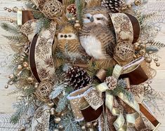 two owls sitting on top of a christmas wreath with pine cones and ribbon around it